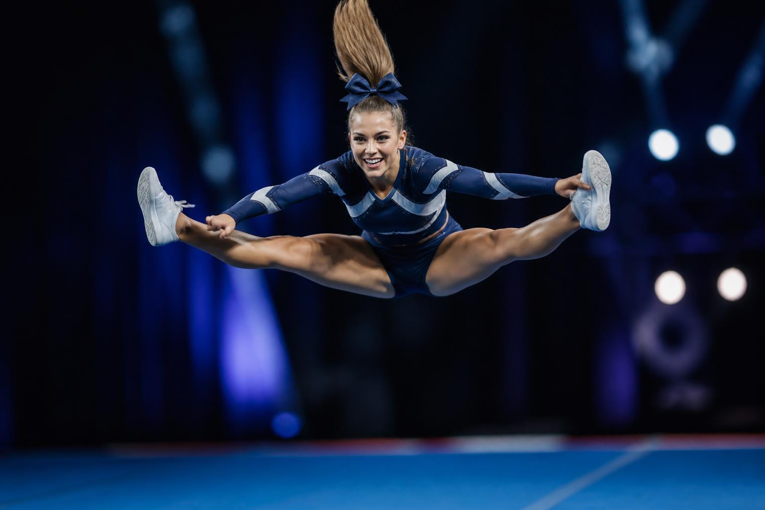 Cheerleader in mid-air toe-touch jump over a competition mat